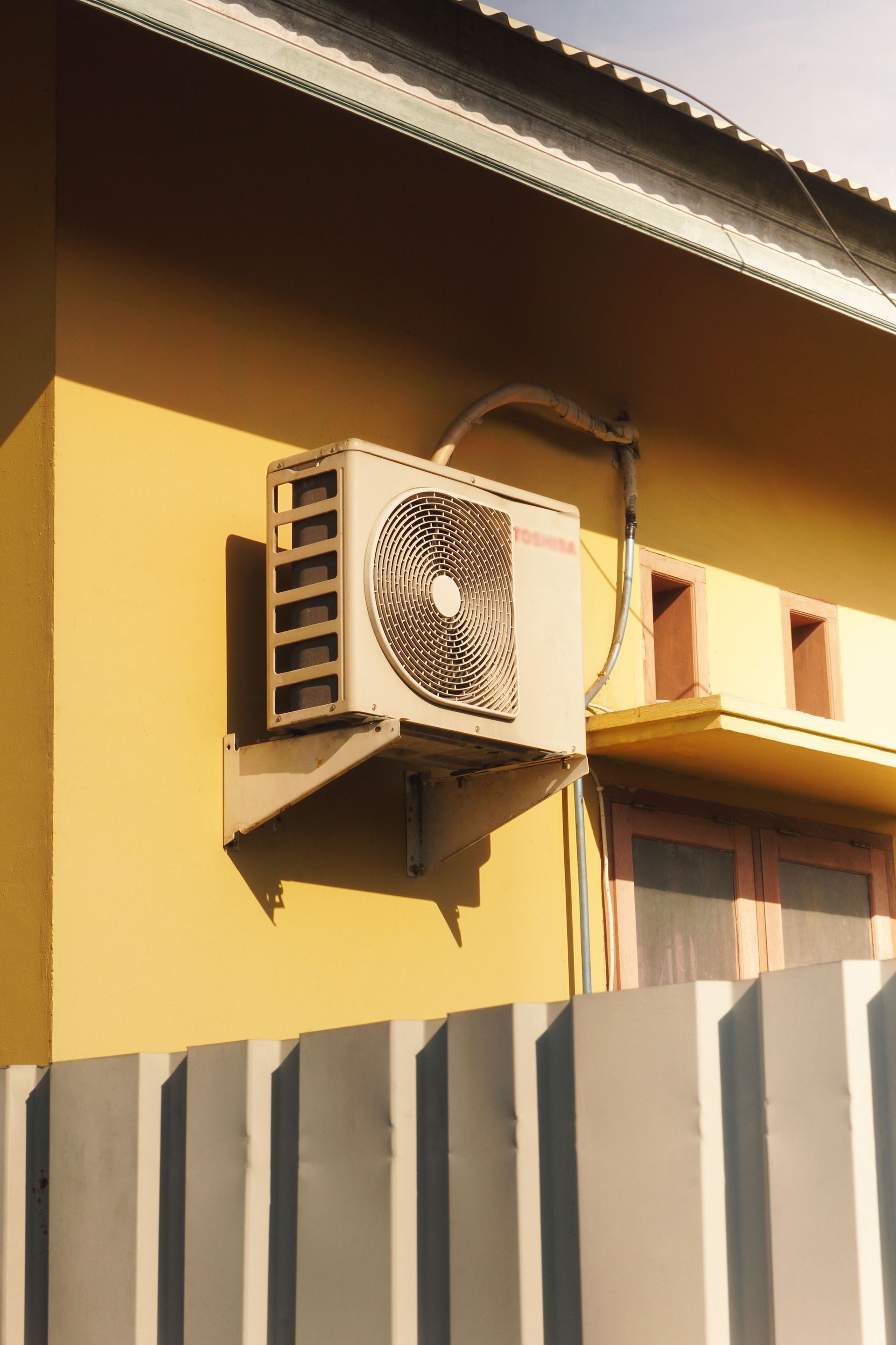 Outdoor air conditioner unit attached to a sunny yellow building facade.